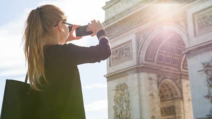 年轻的女游客走在巴黎的街道上并拍摄凯旋门的照片