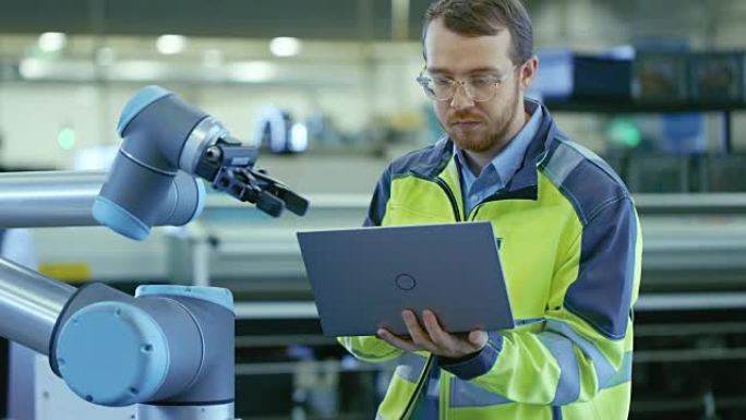 在工厂: 自动化工程师使用笔记本电脑对机械臂进行编程。自动制造业的新时代。