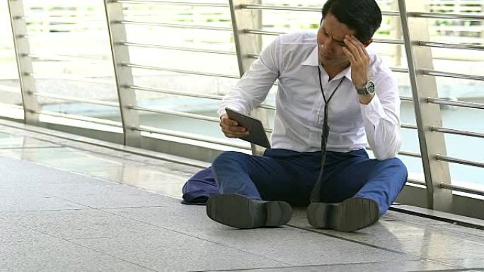 紧张的日间商人坐在地板上时拿着手机。