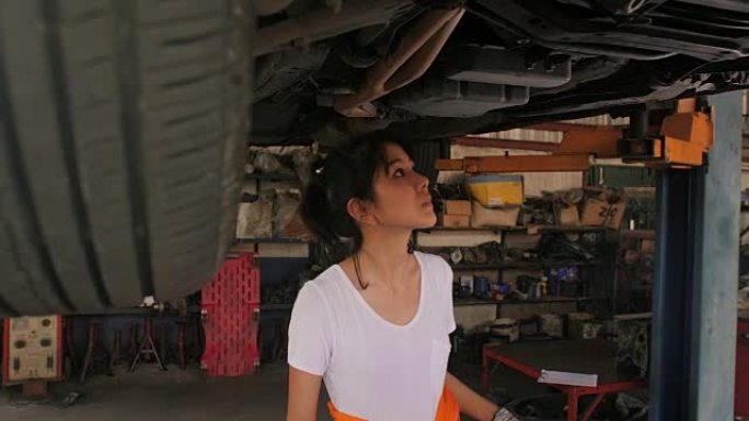 年轻漂亮的汽车修理工在车库里检查汽车底盘路，汽车服务理念。多莉开枪