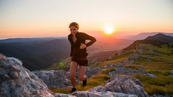 女运动员在日落时在山区的岩石地形上奔跑