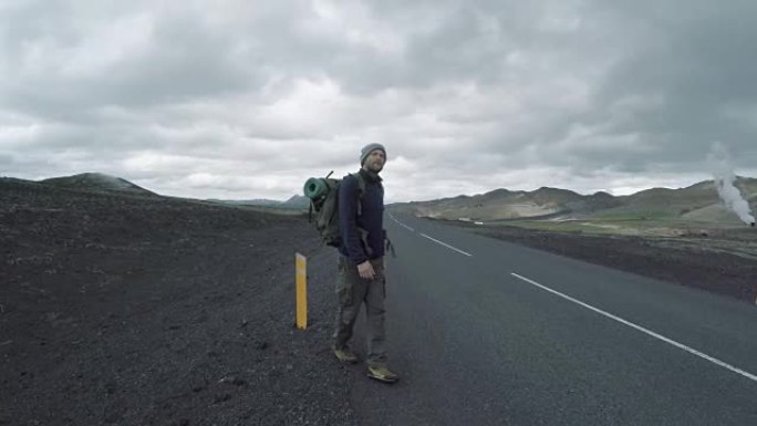 带着背包在冰岛荒凉的道路上行走的游客