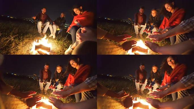 快乐的人们坐在城市背景上的篝火旁。夜间
