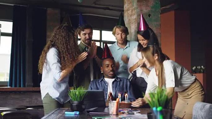 一群年轻人在办公室祝贺非裔美国人生日，带来蛋糕和拍手，盖伊在吹蜡烛，玩得很开心。