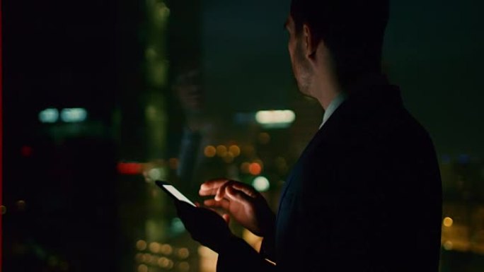 深夜在办公室成功的商人在智能手机上键入电子邮件。在带有城市灯光的商业区窗口中。