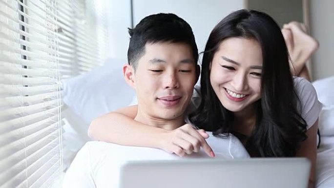 亚洲中国夫妇在卧室里用笔记本电脑上网冲浪