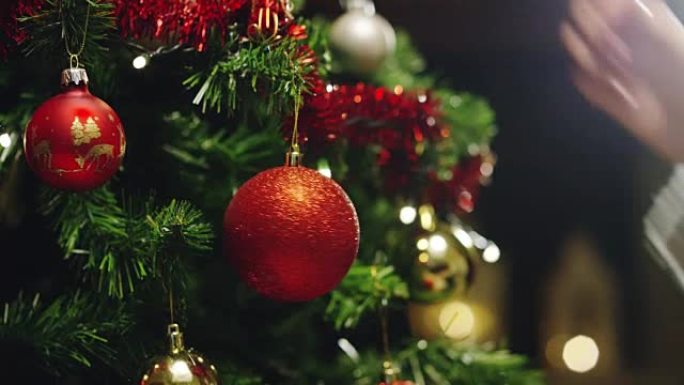 人的手用金色和红色的球装饰圣诞树。等待圣诞节和新年的概念。