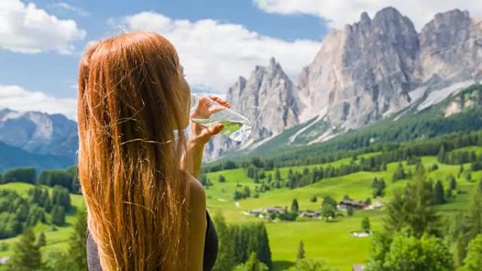 年轻女子徒步旅行，停下来补充水分，欣赏山景