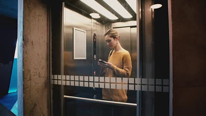 年轻自信的女人进入电梯，按下按钮，关上门，然后使用智能手机移动办公室应用程序骑行