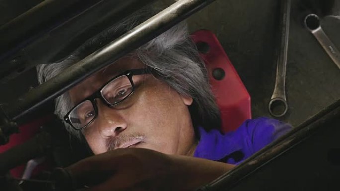 专业的男机械师躺在汽车下面，在车库里修理它。汽车服务理念
