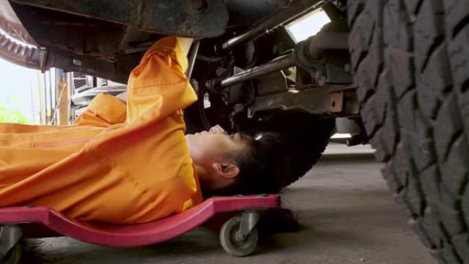 年轻漂亮的汽车修理工正躺在汽车下，在车库里修理它。汽车服务理念。多莉开枪
