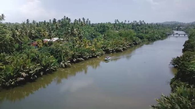 无人机在丛林荒野和热带绿色棕榈树中流动的美丽河流上的白色小船上方左转