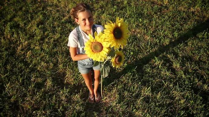 年轻的女孩在日落时拿着向日葵抬头看