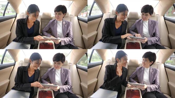 两个女商人坐在汽车后座上，用数字平板电脑聊天