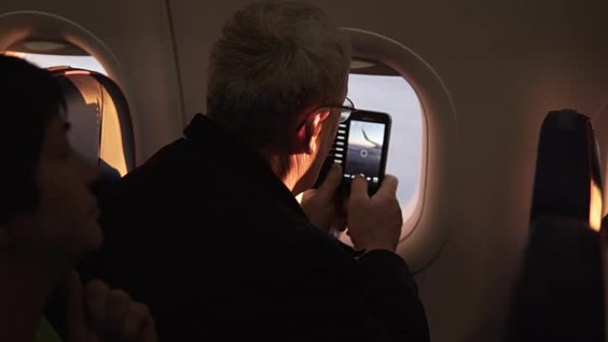 无法识别的高级男性乘客坐在飞机窗户附近飞行时拍摄飞机机翼的智能手机照片