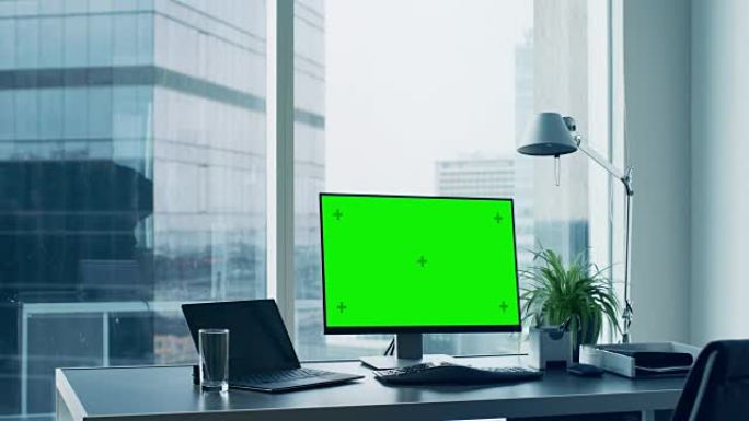 办公桌上的滑动镜头，上面站着绿色的模拟屏幕个人计算机。现代时尚的房间，可以看到大城市商业区的景色。