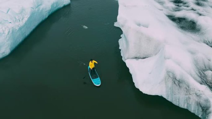 年轻的喜欢冒险的人划着木板在冰岛冰川湖的冰山上冲浪