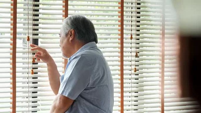 退休男子独自在家。悲伤的老人独自站在窗户旁思考: 自然采光镜头中的悲伤和沮丧