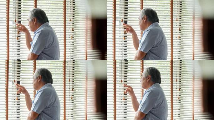 退休男子独自在家。悲伤的老人独自站在窗户旁思考: 自然采光镜头中的悲伤和沮丧