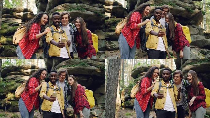 快乐的非裔美国人家伙正在与朋友一起在森林徒步旅行期间使用智能手机进行视频通话，年轻人正在看着屏幕，挥