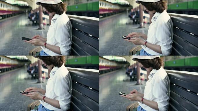 旅行者背包客亚洲女人在泰国曼谷旅行。快乐的年轻女性坐在长凳上，使用智能手机在火车站聊天，阅读和发短信