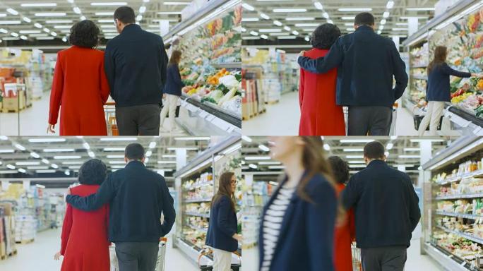 在超市: 幸福的年轻夫妇走过商店的新鲜农产品区，男人深情地拥抱女人。拍摄后的后视图。
