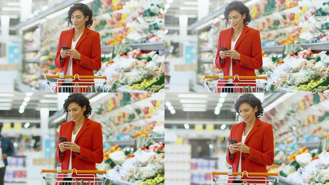 在超市: 美丽的年轻女子站在商店的新鲜农产品区时使用智能手机。