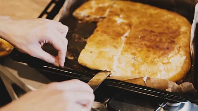 女厨师手的特写镜头试图用刀从厨房托盘上取下粘性的自制馅饼