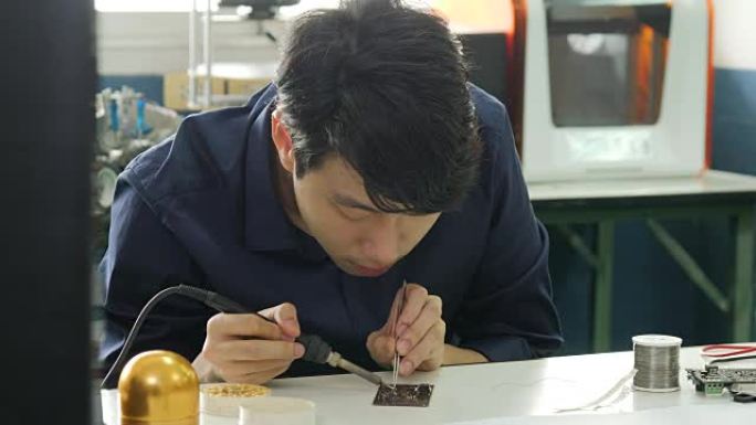 亚洲电子工程师正在他的车间焊接电板。亚洲学生正在教室里学习电子和焊接。