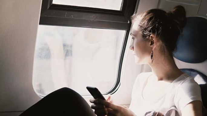 美丽的和平的欧洲女孩使用智能手机应用程序在火车上旅行，键入消息，看着窗户