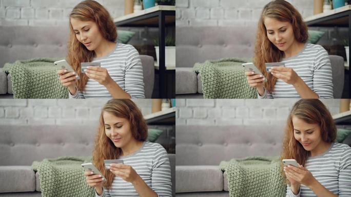 漂亮的年轻女子正在网上购物，使用智能手机用银行卡支付购物费用，女孩拿着卡，输入信息触摸屏，然后微笑。