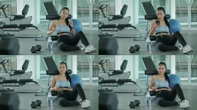 年轻的运动女人在健身房的智能手机上听音乐。艰苦锻炼后休息