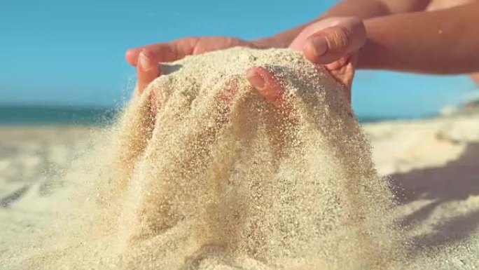慢动作: 女人舀起一把沙子，在手指之间筛分。
