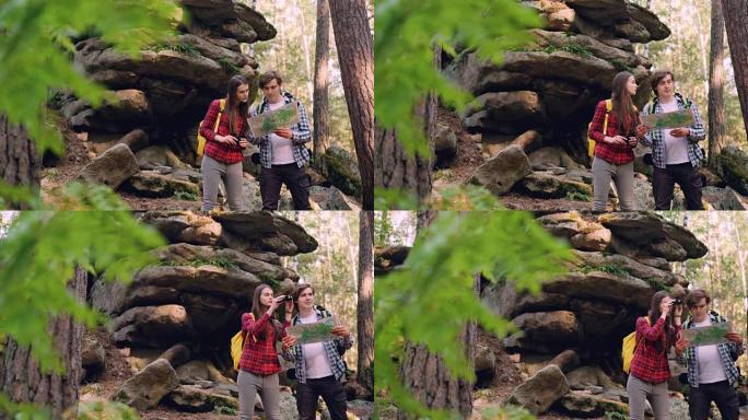 迷路的游客站在巨大岩石附近的森林中，然后通过双筒望远镜查看地图，并讨论前往目的地的方式。人与自然的概