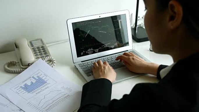女商人在文件纸和笔记本电脑屏幕上查看财务图表，4K(UHD)