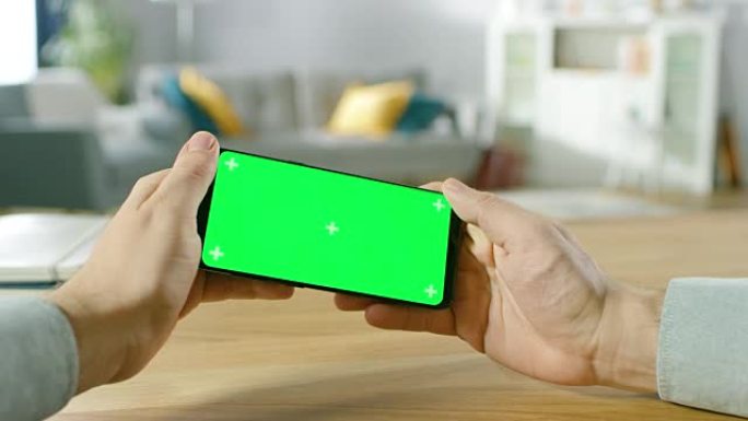 该男子的第一人称特写镜头，该男子在横向模式下手持绿屏智能手机，并通过倾斜手机在赛车视频游戏中玩游戏。