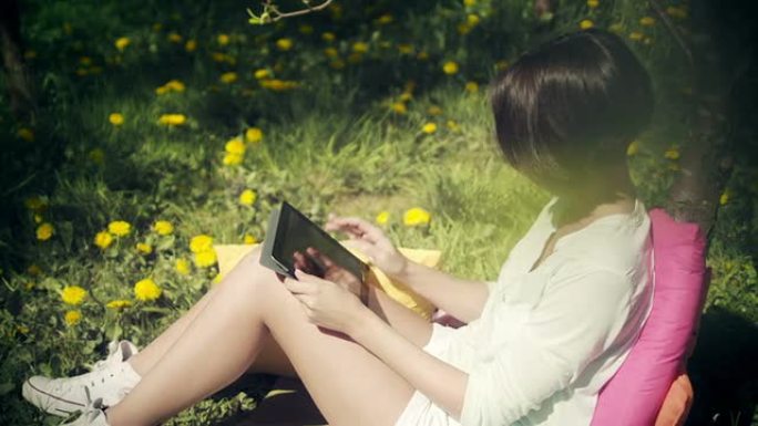 女人在阳光明媚的日子在花园里使用平板电脑