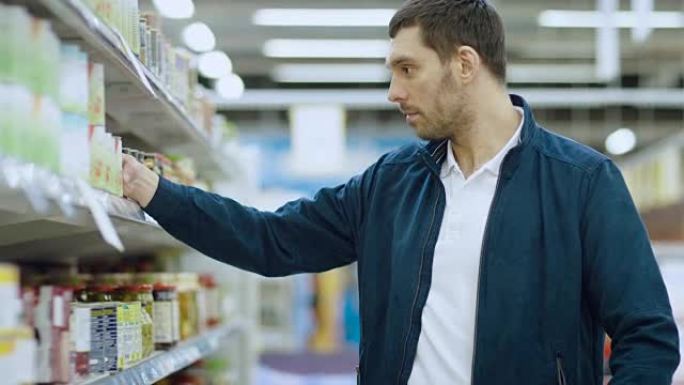 在超市:英俊的男人浏览货架上的罐头商品，把锡罐放进他的购物车，继续他的购物清单走过不同的部分。