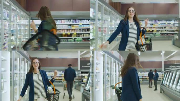 在超级市场:美丽的年轻女人拿着购物篮在商店的冷冻商品和乳制品区跳舞。