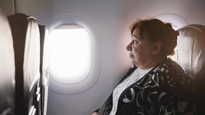 欧洲高级女飞机乘客坐在飞机靠窗的座位上，紧张又害怕飞，环顾四周