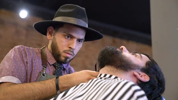 沙龙中年轻的理发师修剪客户的胡须