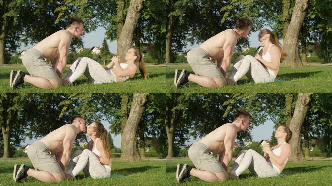 慢动作: 开朗的情侣接吻，而年轻女子在公园里仰卧起坐。