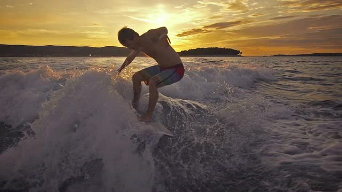年轻人在日落时在船后冲浪