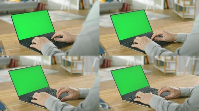 专业的自由职业者坐在他舒适的客厅的桌子旁，在带有绿色模拟屏幕的笔记本电脑上工作。