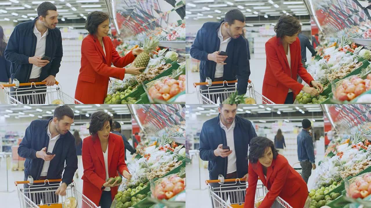 在超市: 幸福的夫妇购物，在新鲜农产品区选择水果和蔬菜。男人使用智能手机并推动购物车，女人将产品放入