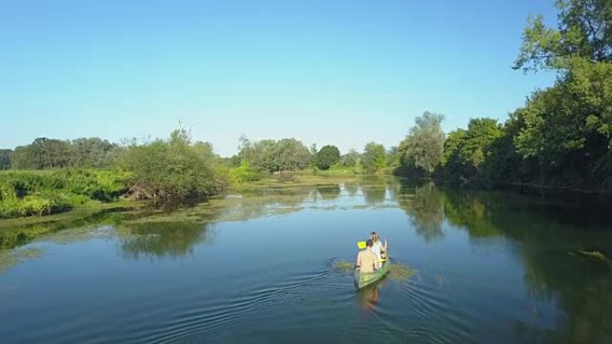 空中: 活跃的年轻夫妇将独木舟划过一条宁静的深蓝色河。