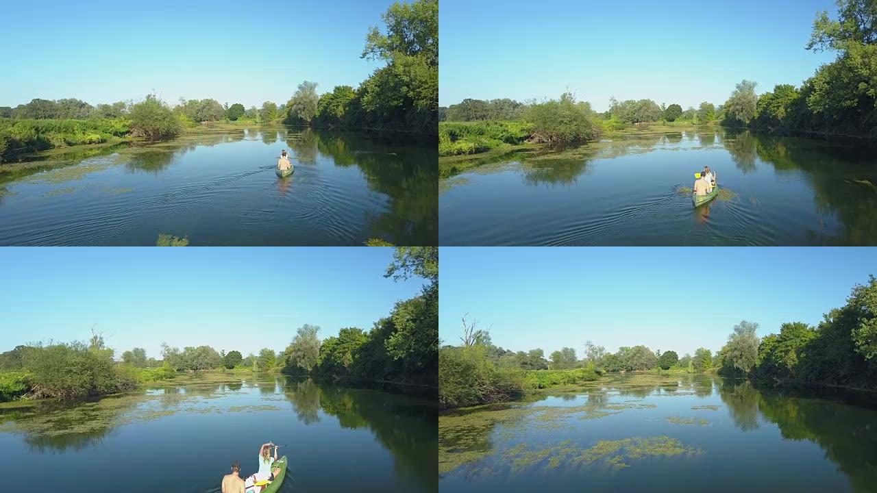 空中: 活跃的年轻夫妇将独木舟划过一条宁静的深蓝色河。