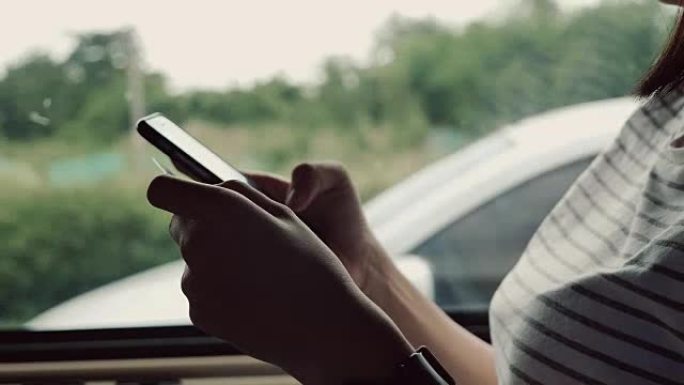 亚洲妇女坐在汽车后座上，用信用卡使用电话