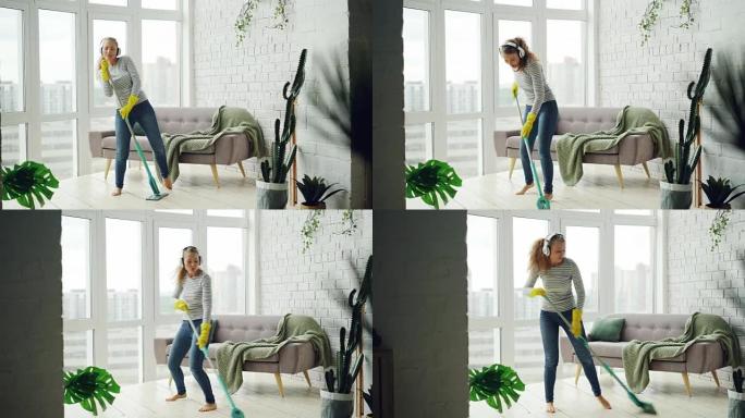 快乐的女孩在轻便的公寓里拖地板，通过耳机听音乐、跳舞和唱歌很开心。美丽的家具和植物是可见的。