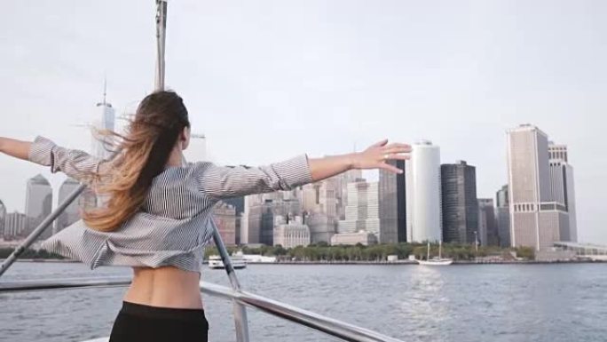 美丽兴奋的旅行者女孩，头发飞扬，双臂张开，在旅游船上观看纽约天际线慢动作